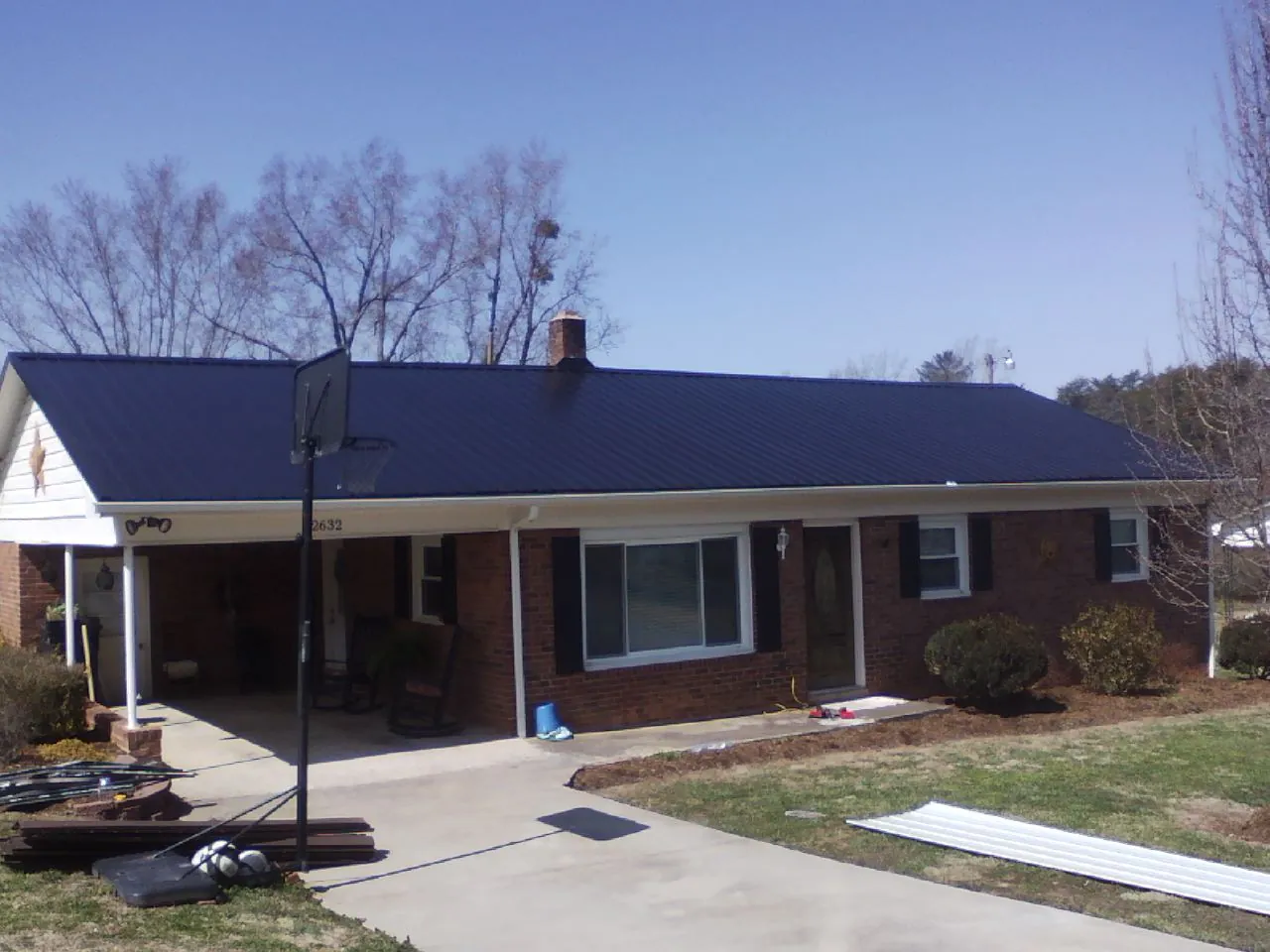 Finished dark blue metal roof on a brick ranch with a carport in Lenore