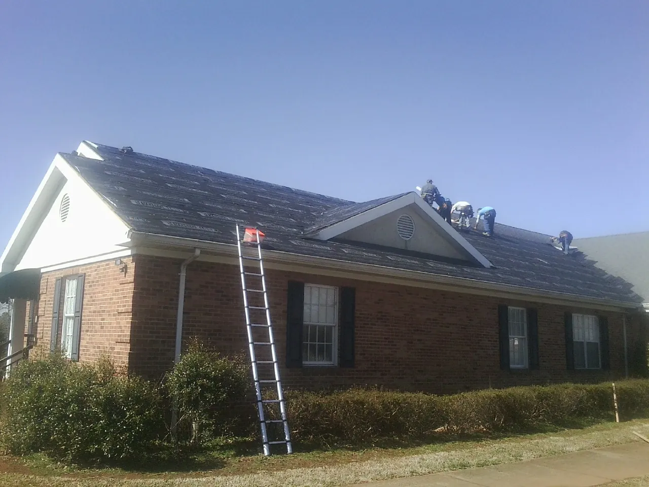 Crew tearing shingles off a brick ranch roof with a ladder set — Emergency Roof Repair work by our crew in Lenore