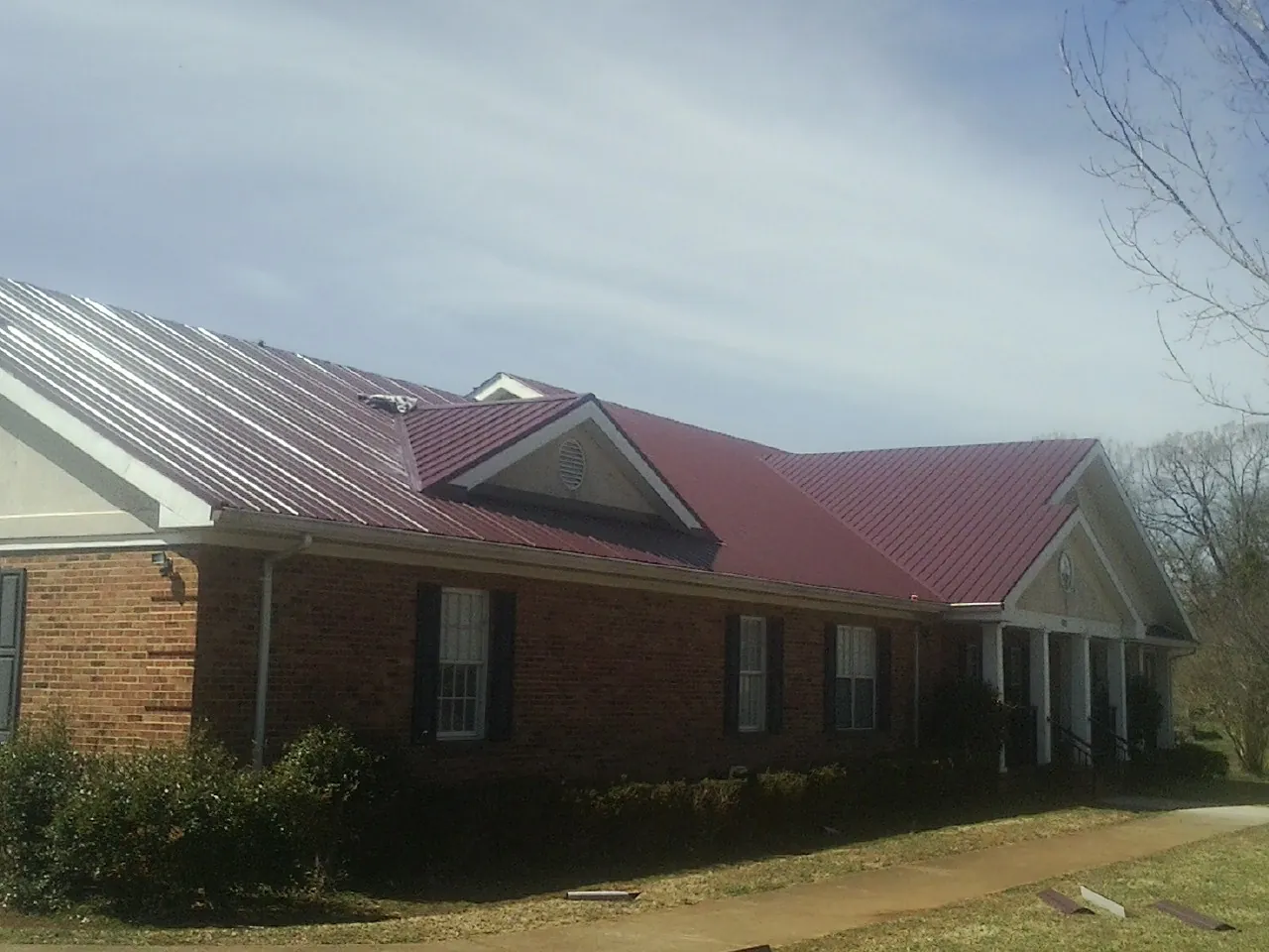 Red metal roof with gabled entries on a long brick building, from a Hail Damage Roof Repair job in Lenore