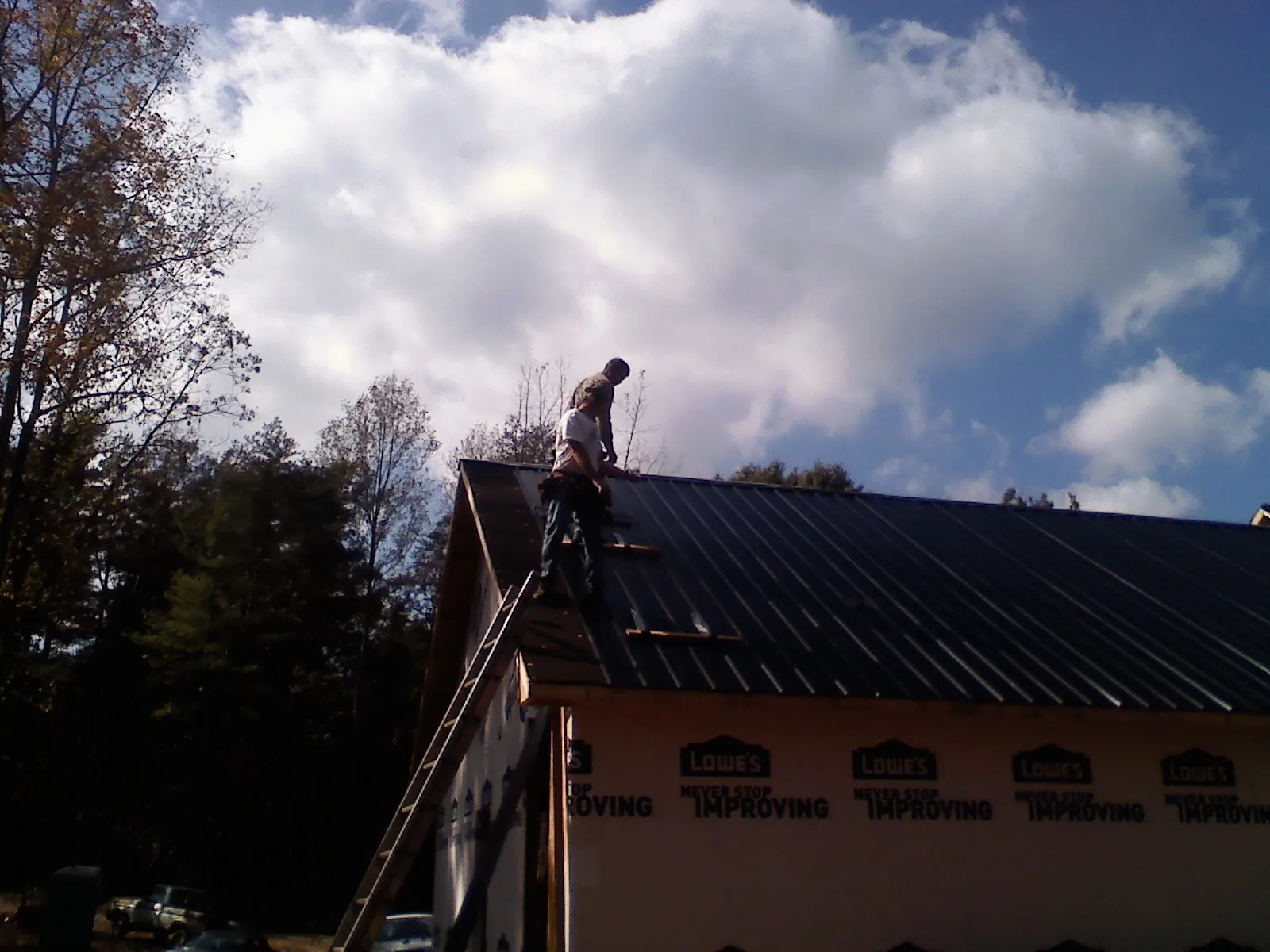 Roofer fastening dark metal panels high against a cloudy sky, from a Roof Inspection job in Lenore
