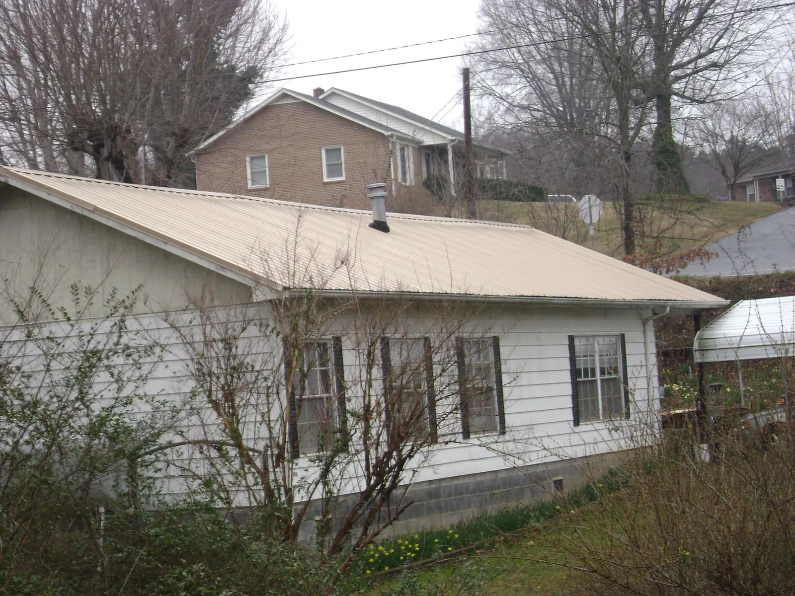 Tan metal roof on a white sided house set into a hillside — Commercial Roofing by Roofing Brothers in Lenore