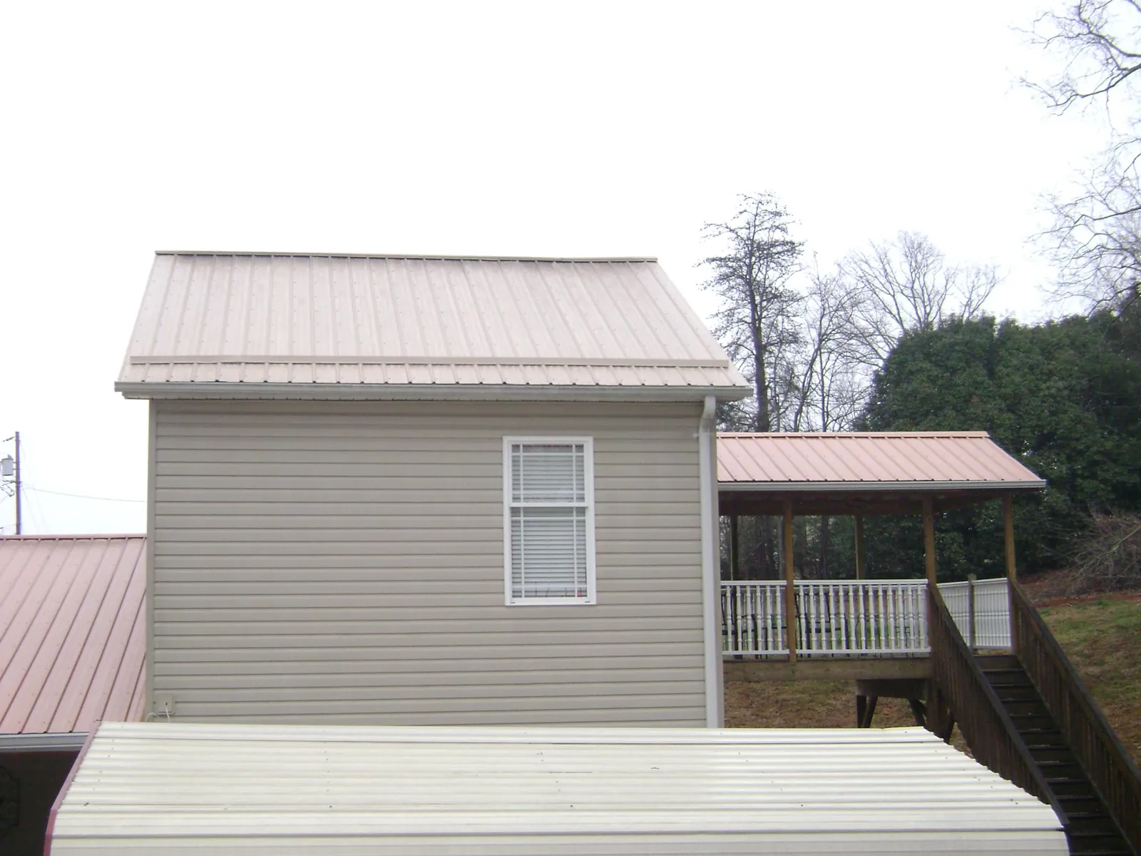 Tan metal roofs on a two story addition and attached porch, from a Roof Replacement job in Lenore